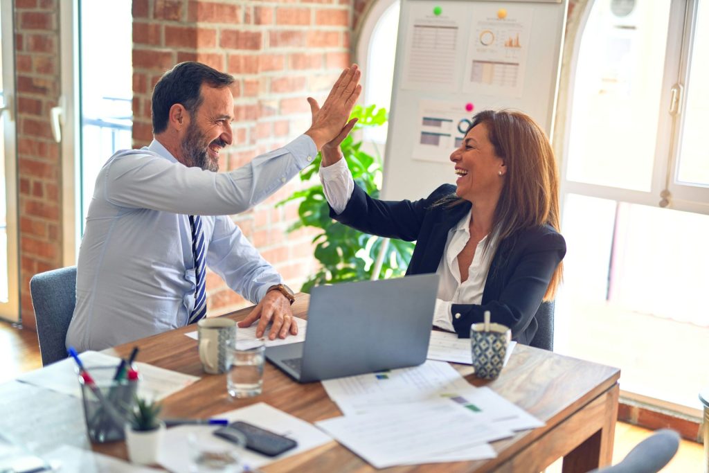 A business man and woman giving each other a high five with business documents scattered around them.
