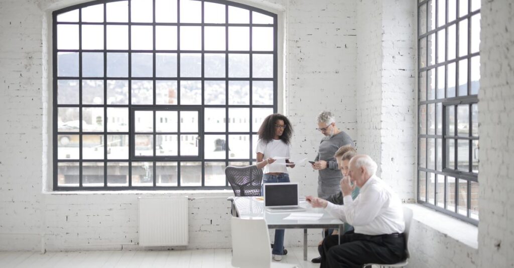 Colleagues collaborating in a bright industrial office space with large windows.