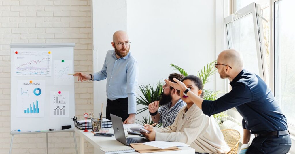 A group of professionals engaged in a business meeting, discussing financial graphs on a whiteboard.