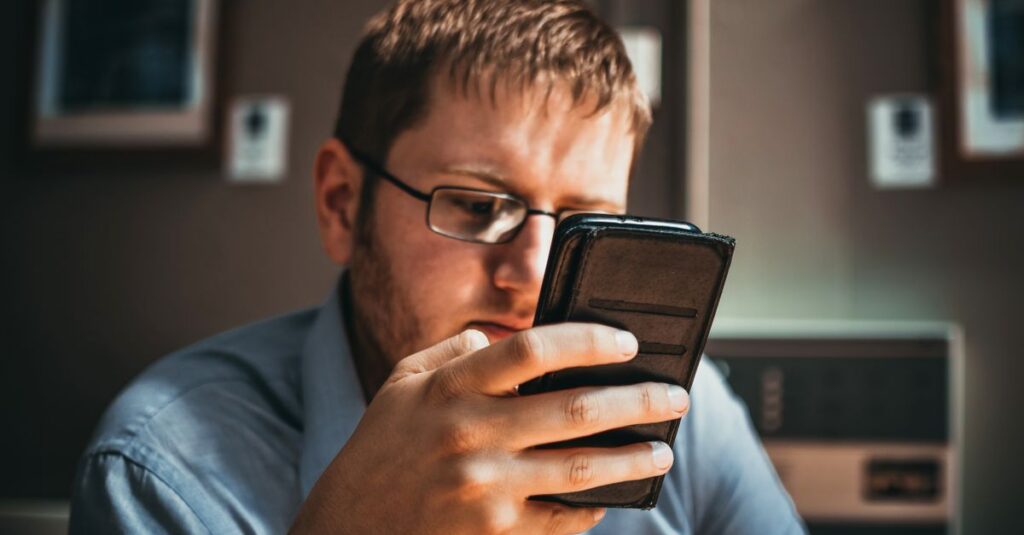 Serious businessman wearing glasses focused on smartphone in a modern office setting.