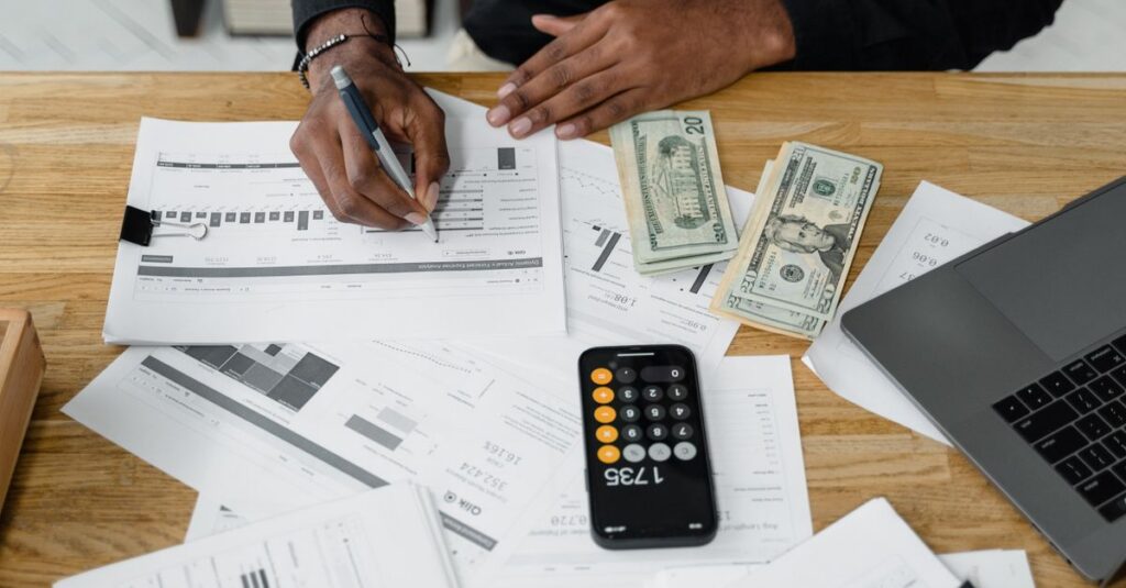 Man working on financial reports with calculator, money, and laptop on a desk.