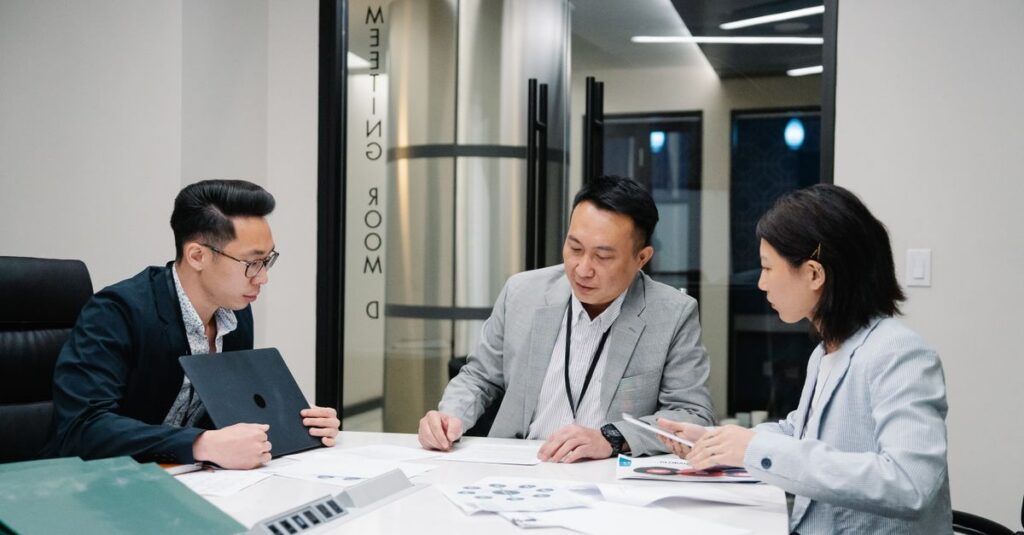 Business meeting with three professionals collaborating in a modern conference room setting.