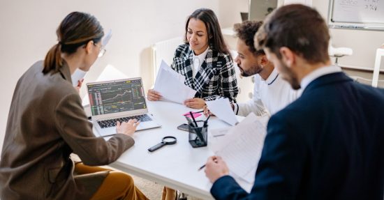 A team of diverse professionals collaborating and analyzing data on a laptop in an office meeting.