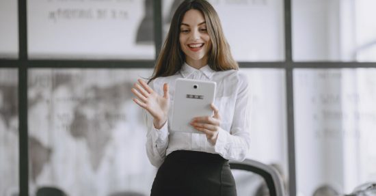 A smiling brunette woman in a professional office setting using a digital tablet for work.