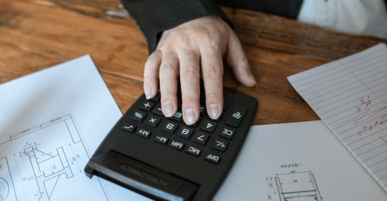 Hand using calculator for architectural calculations on blueprints.