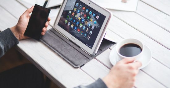 Person using a tablet and smartphone at a table with coffee, showcasing a digital workspace.