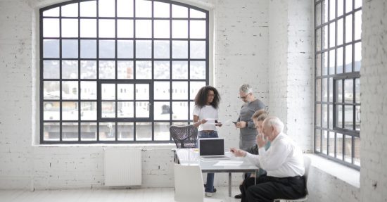Colleagues collaborating in a bright industrial office space with large windows.