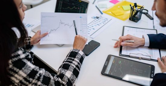 Two colleagues analyzing financial graphs during a business meeting in a modern office setting.