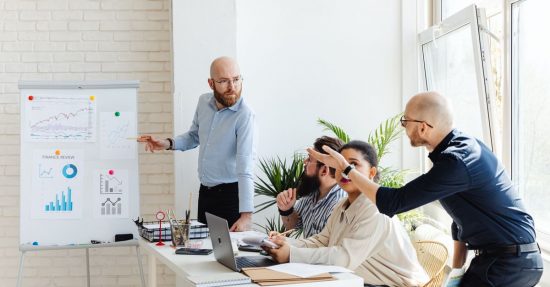 A group of professionals engaged in a business meeting, discussing financial graphs on a whiteboard.
