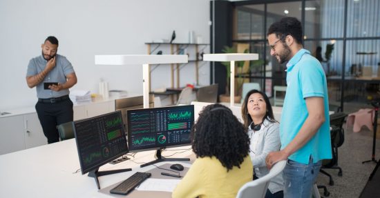 Office employees collaborate on financial data at modern workspace, engaging in teamwork and communication.