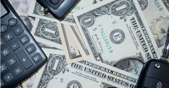 An arrangement of US dollar bills, car keys, and a calculator representing finance and investment concepts.