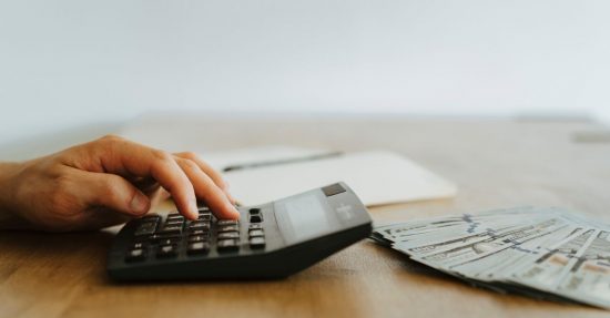 A hand calculating finances with a calculator next to stacks of US dollar bills.