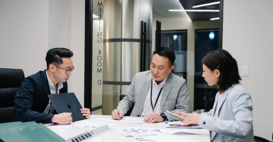 Business meeting with three professionals collaborating in a modern conference room setting.
