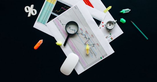 Overhead view of an office desk with financial documents, a magnifying glass, and stationery items, suggesting business analysis.