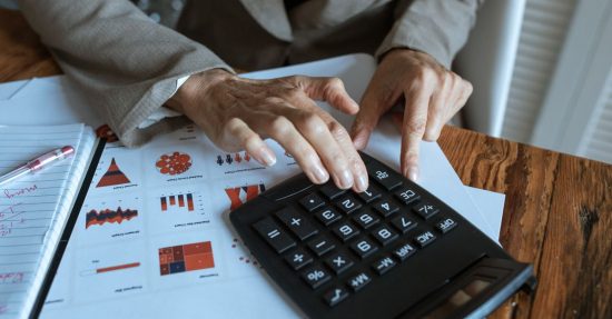 A businessman using a calculator to analyze financial charts and graphs on a desk.