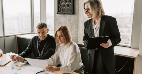 A group of business professionals discussing documents at a conference table in a modern office environment.